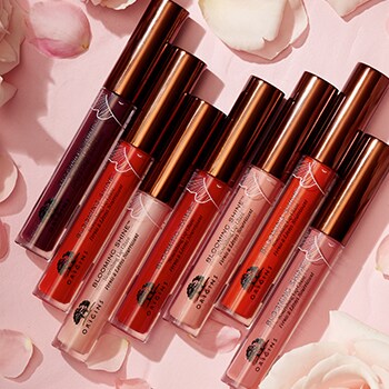 seven blooming shine lip glaze tubes on pink background and flower petals